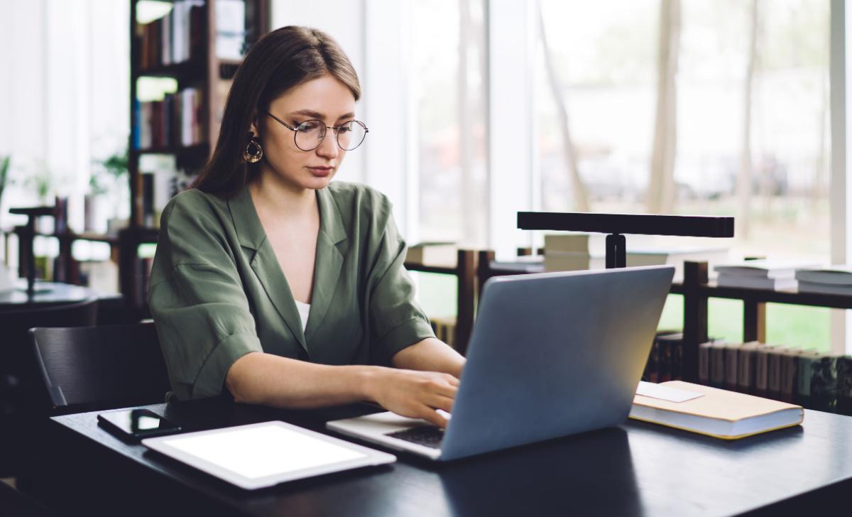 Girl in a green blazer types on her laptop in a library