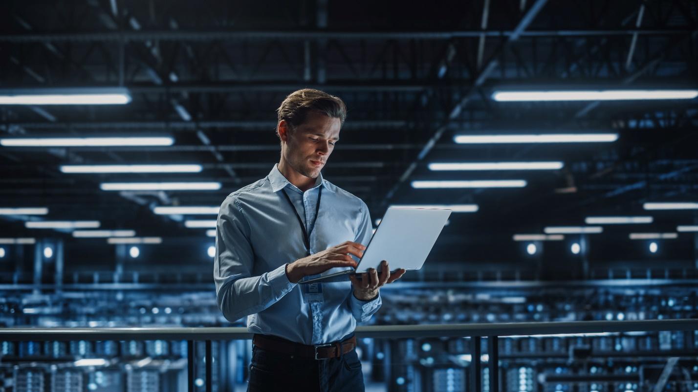 An IT professional with a laptop standing by a group of servers.