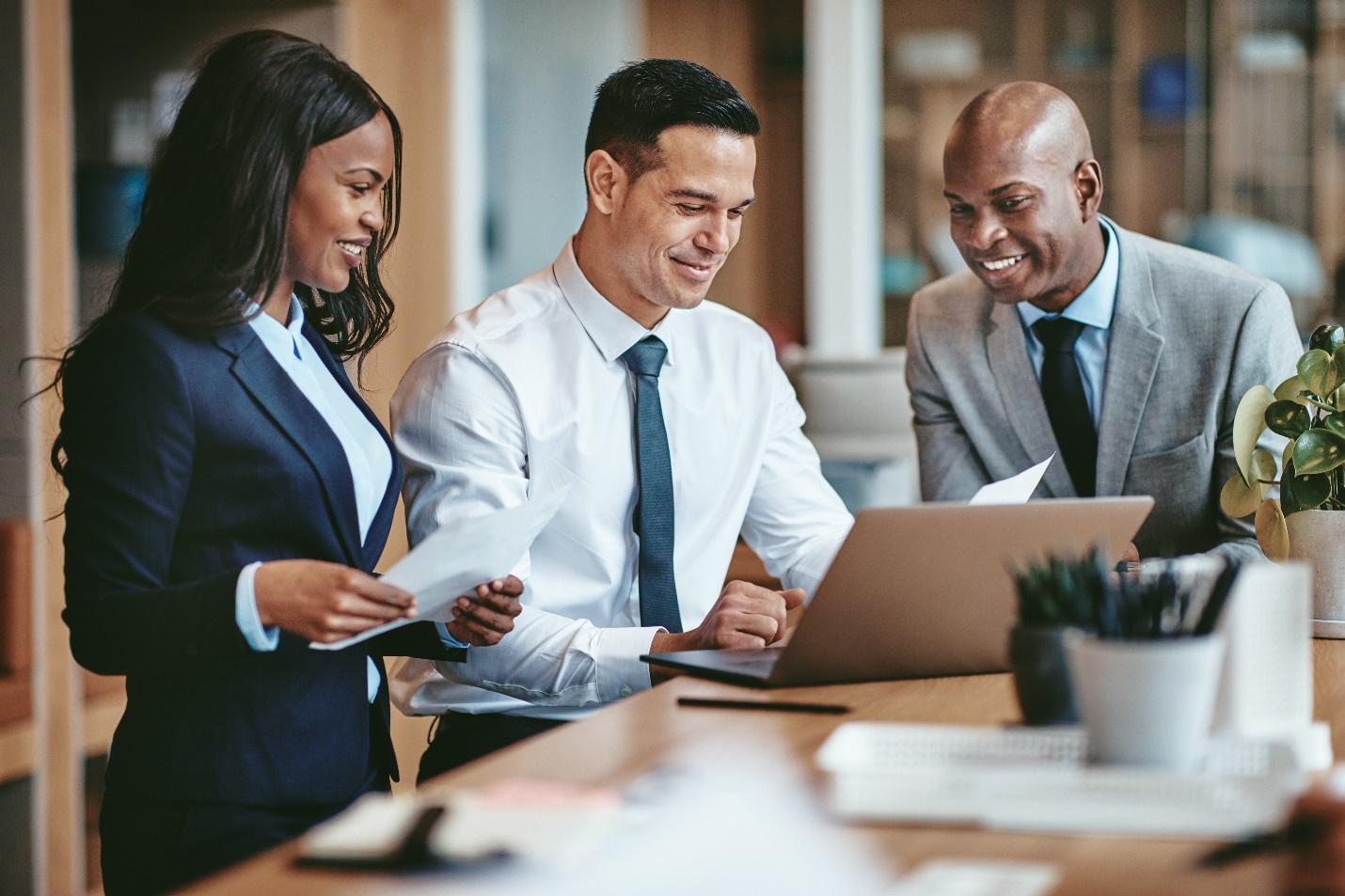 Three IT professionals examining data on both a laptop and a sheet of paper.