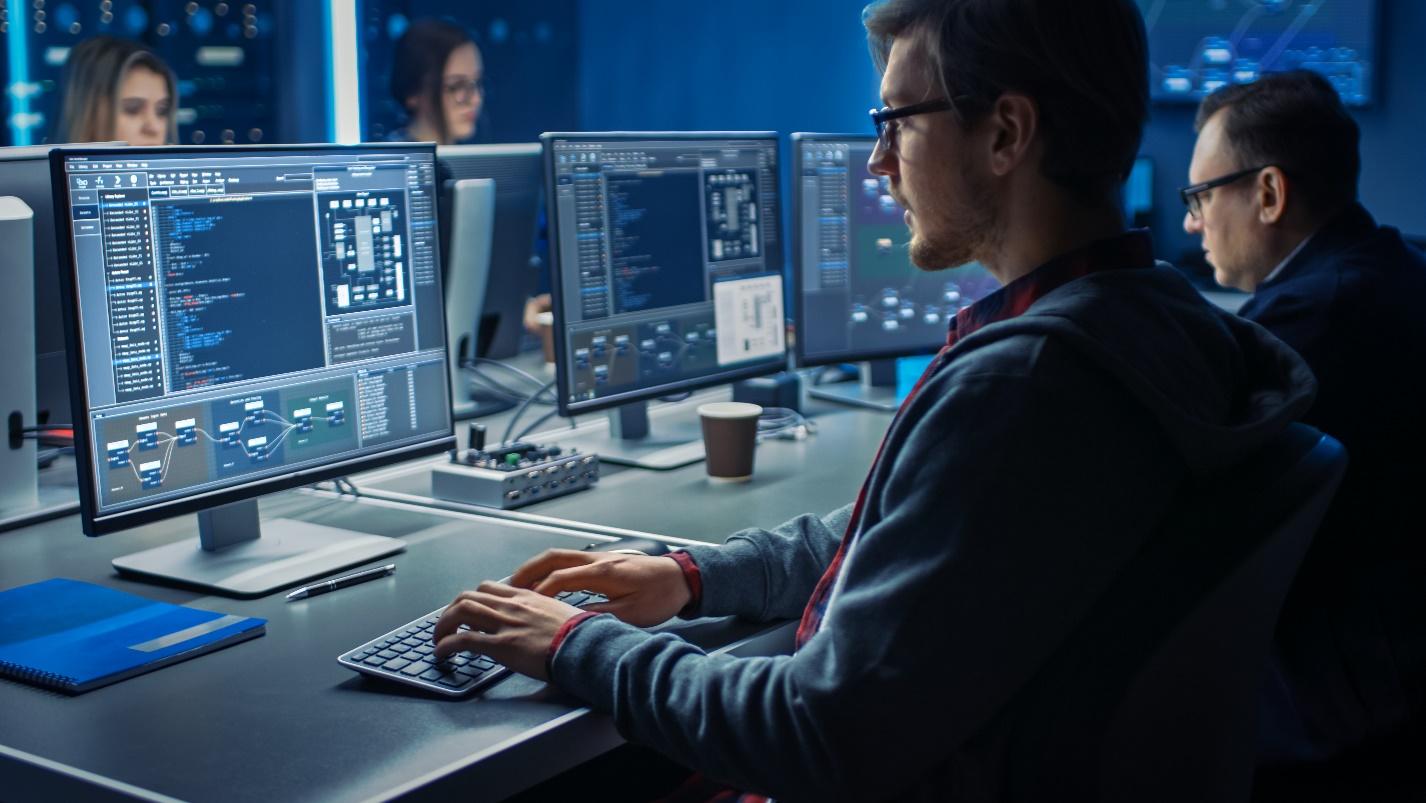 Four IT professionals monitoring code on desktop computers.