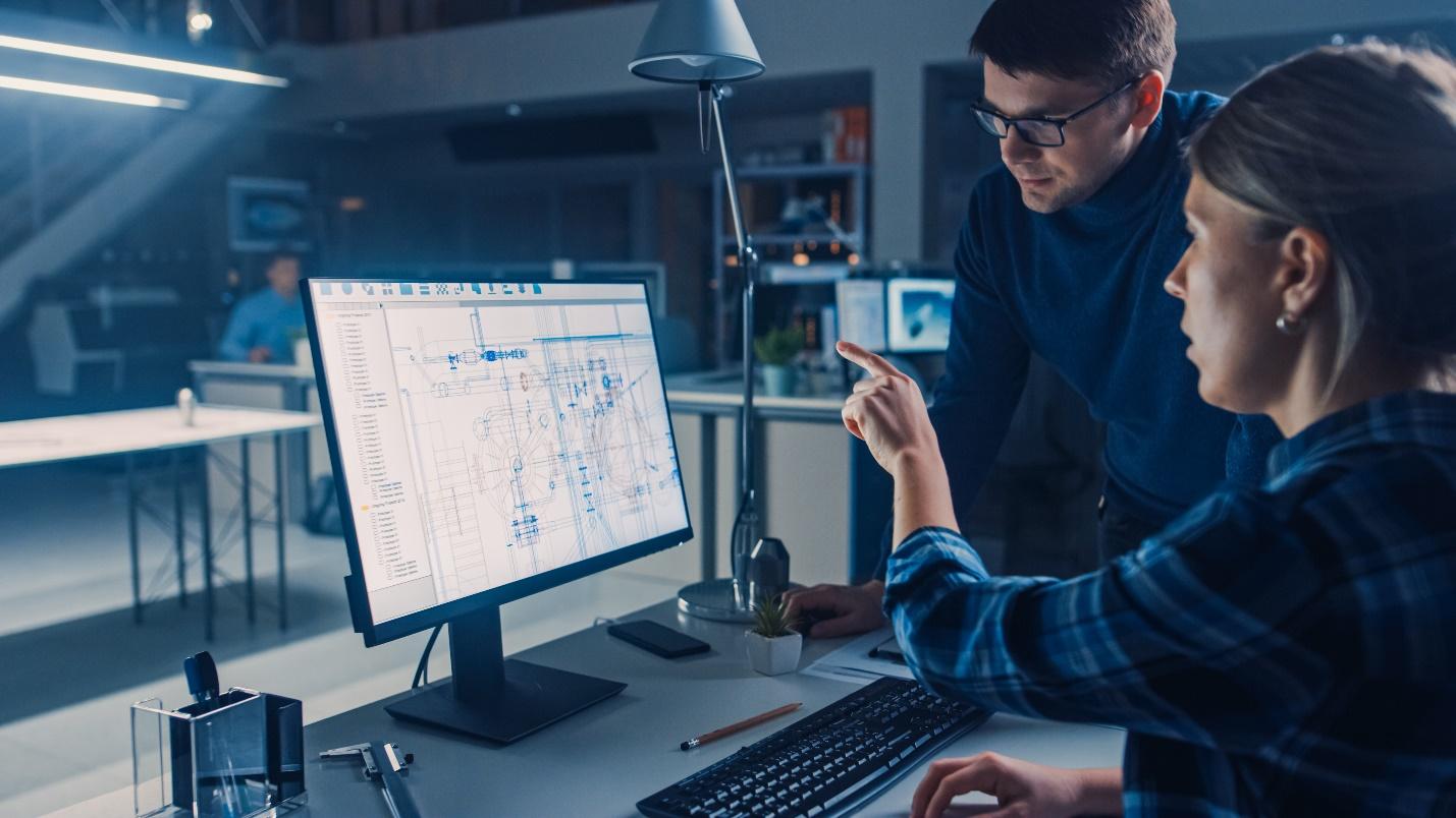 Man and woman at a desk with a computer monitor discussing information on the screen about software.