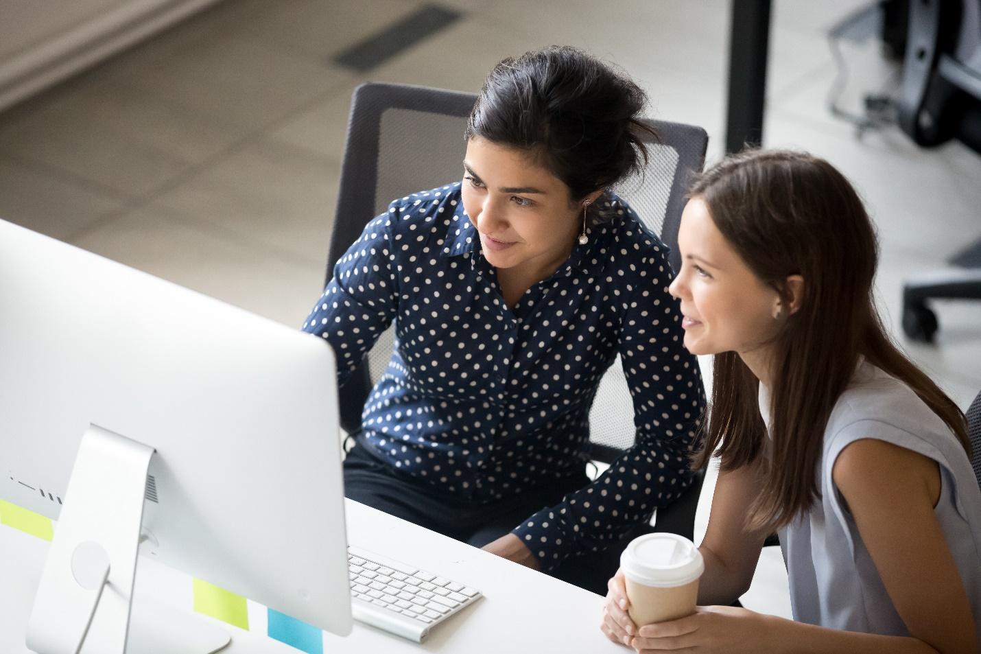 Two women sitting at a desk looking at a computer.