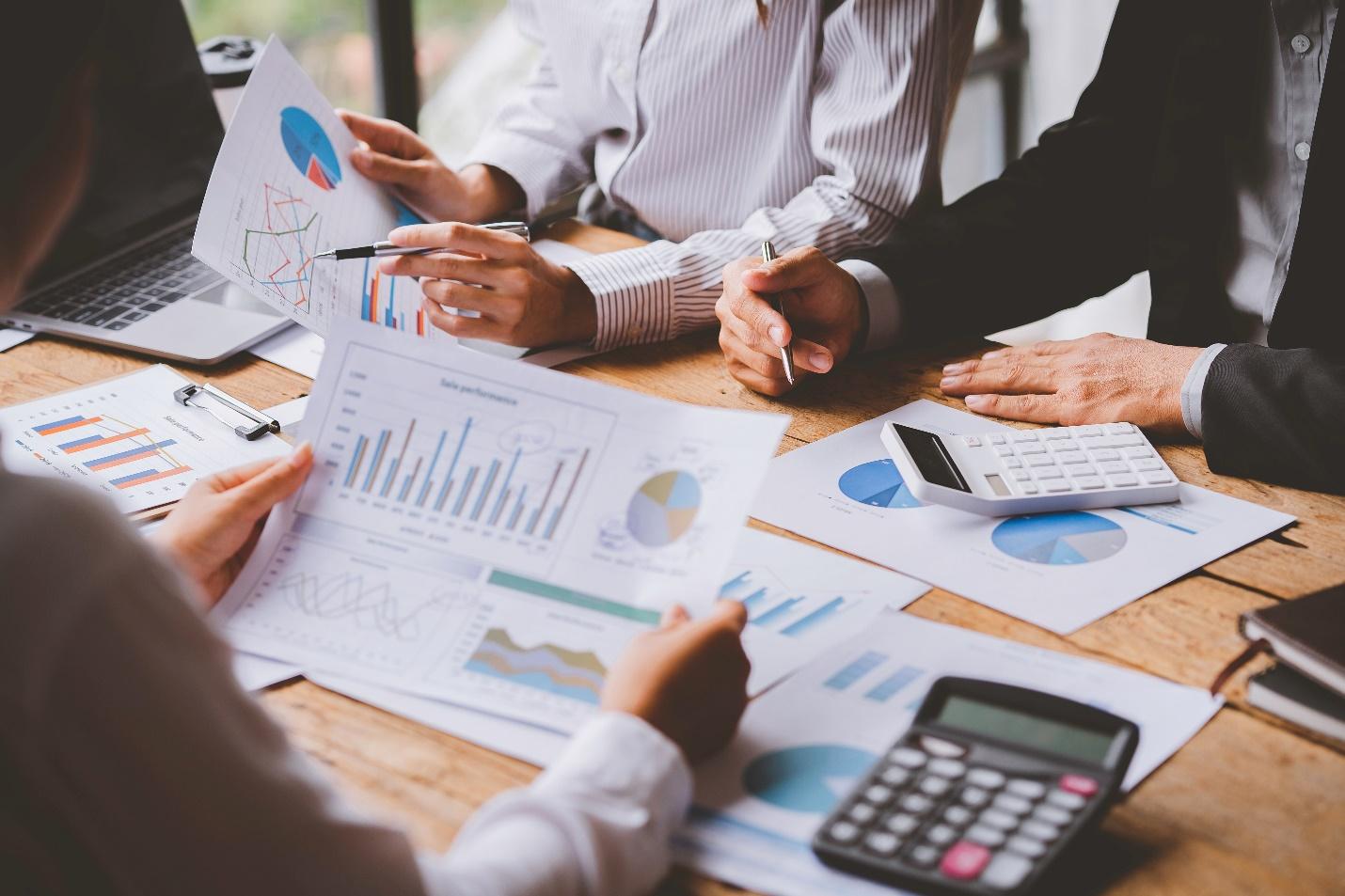 Detail image of three business professionals around a conference desk looking at various charts and using a calculator.