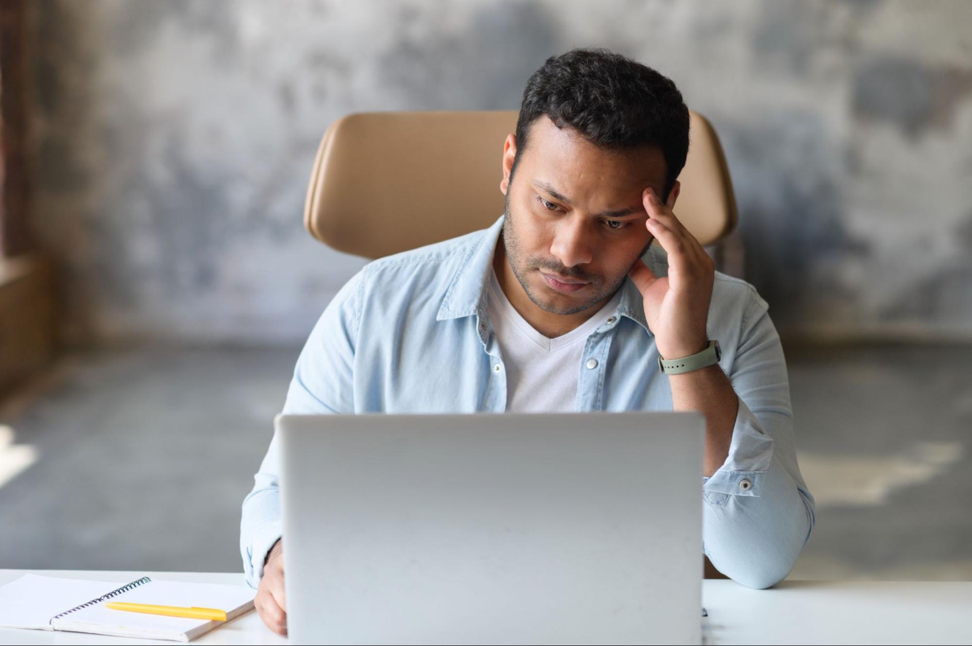 A frustrated man working at a laptop.