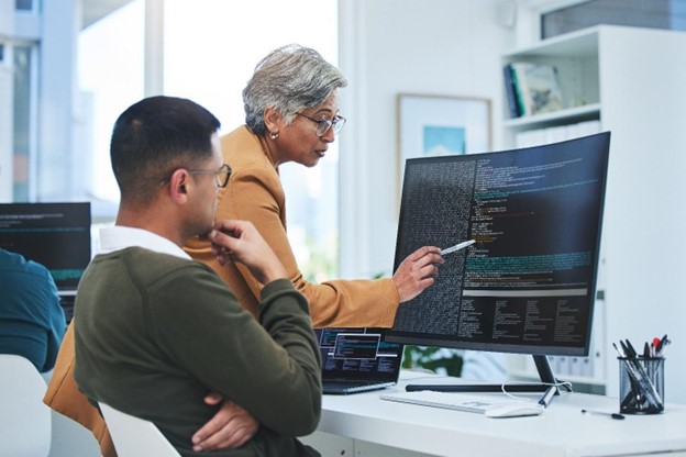 A standing woman points out something on a computer monitor to her seated colleague.