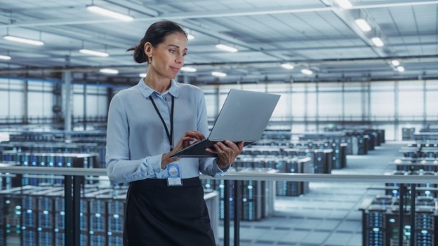 A cybersecurity expert engrossed in analyzing data on their computer, standing in a data center.