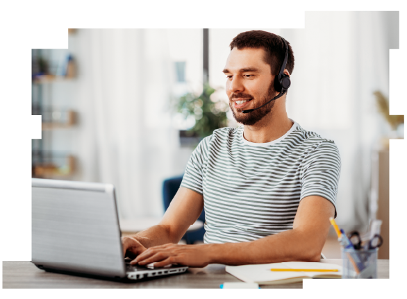 A smiling man wearing a headset and sitting at a table typing on a laptop