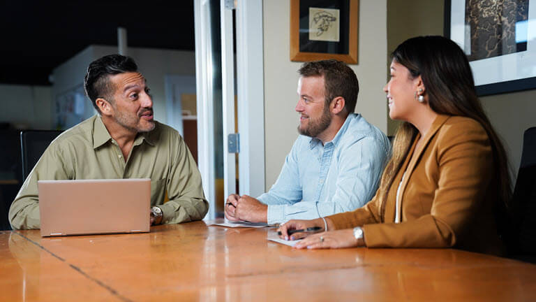 person with laptop open talking to two other people at a conference table